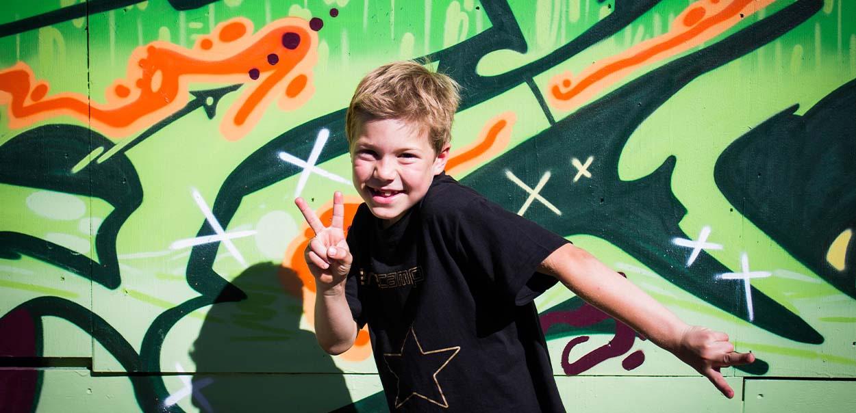 Barn poserer foran graffitivæg 