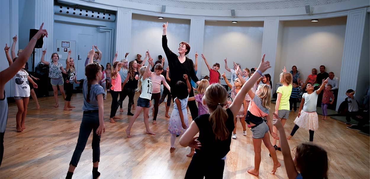 En masse børn som danser og peger mod loftet