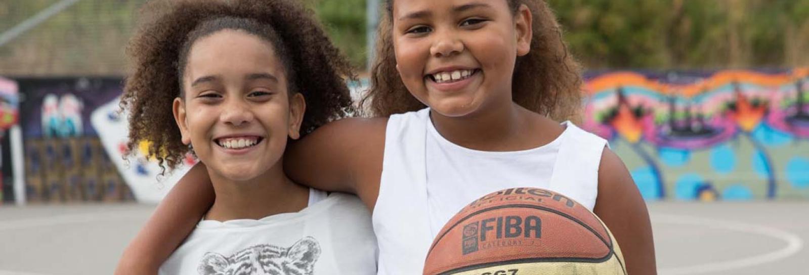 To piger, der står skulder ved skulder med en basketbold
